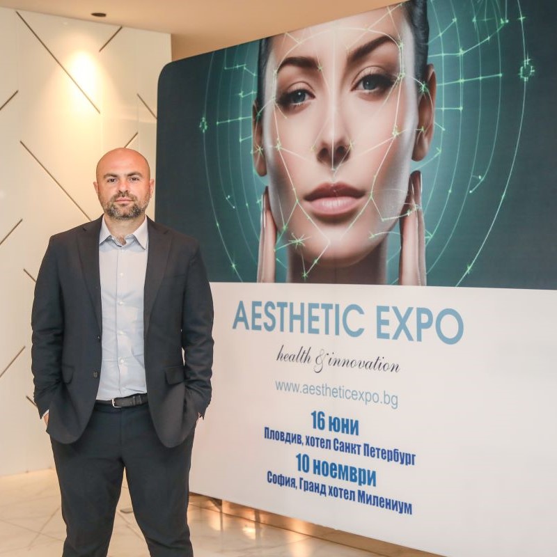Мъж стои пред реклама на Aesthetic Expo с дата и информация за събитието.