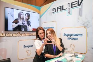 Две жени правят сърце с ръце на щанд на изложение с логото на SALEV.