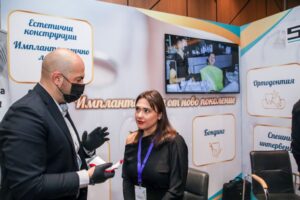 Мъж в черен костюм говори с жена на събитие за стоматологични импланти.