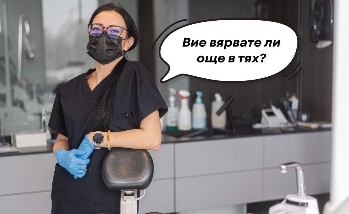 Зъболекар в черна униформа с маска и ръкавици, стояща в стоматологичен кабинет.