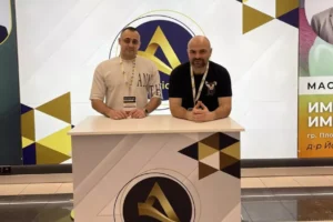 Двама мъже стоят на стойка на Apriori на събитие с графичен фон.